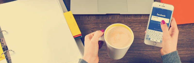 Hand holding cup of coffee and other hand holding phone on Facebook.